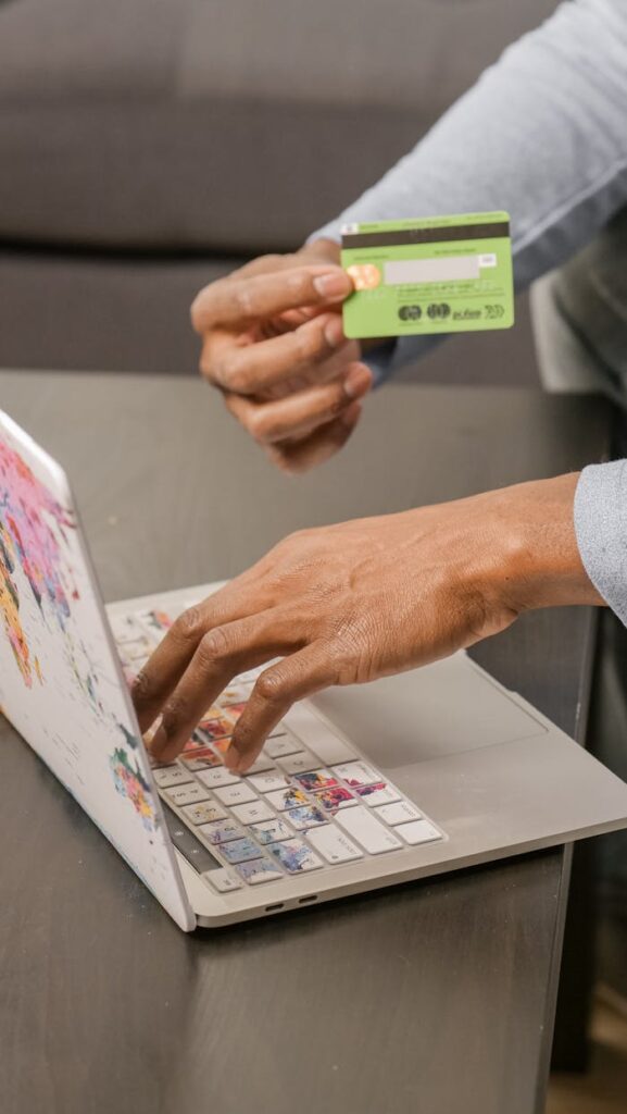 Photo of a Person's Hands Holding a Credit Card Near a Laptop